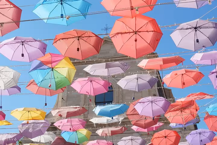 Colorful umbrellas hang above a Catania street, creating a vibrant canopy against a clear blue sky.