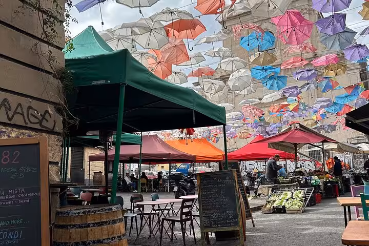 Colorful umbrellas hanging above a lively outdoor market in Catania, offering a unique street food and shopping experience.