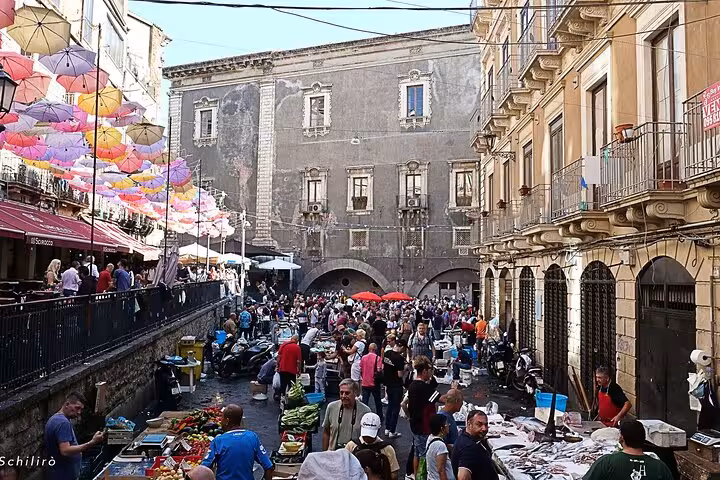 Vibrant Catania street market with colorful umbrellas and crowds, offering a lively atmosphere and local street food experiences.