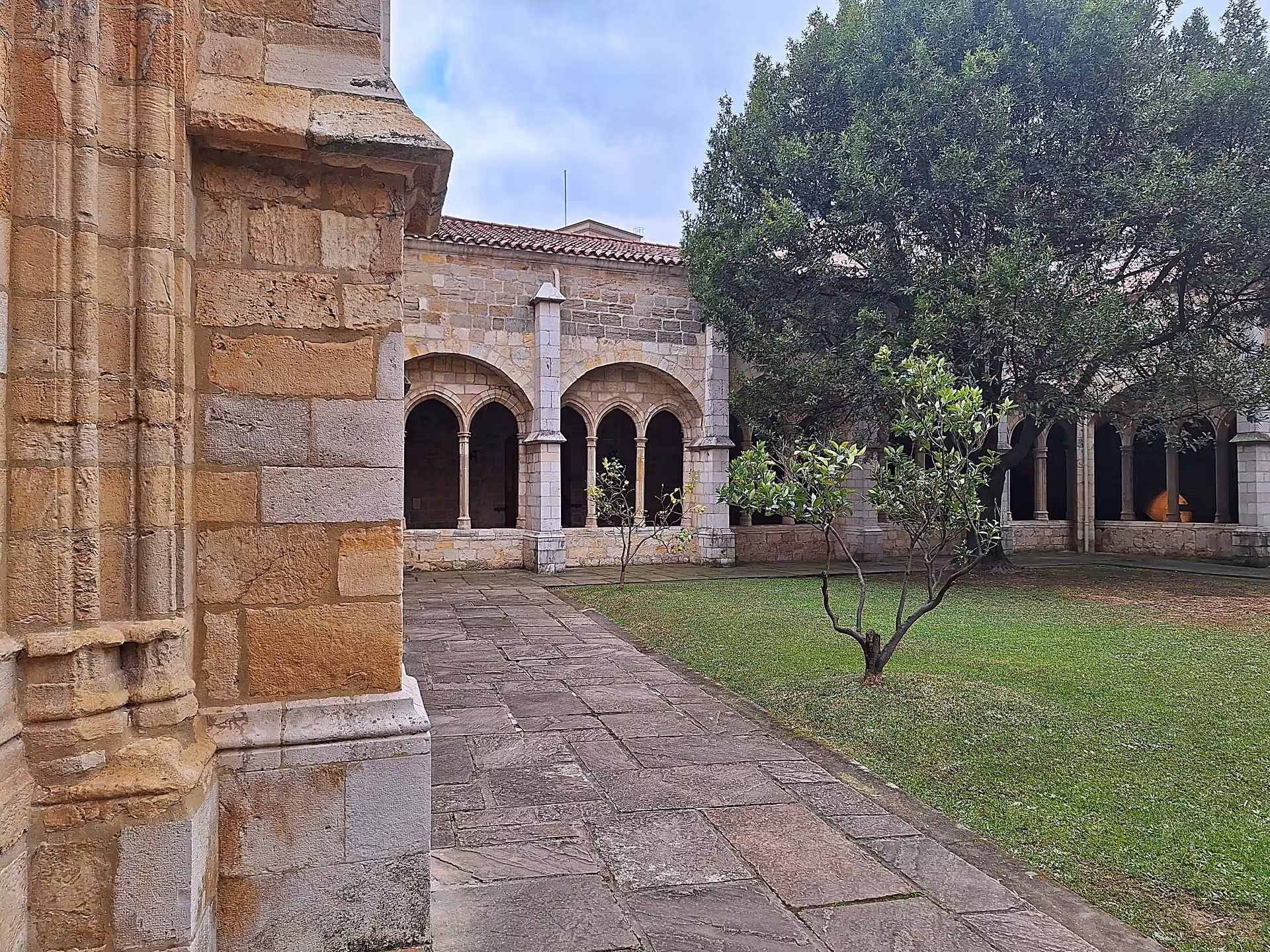 Discover the serene cloister garden of the Cathedral of Santander, featuring lush greenery and historic stone arches.