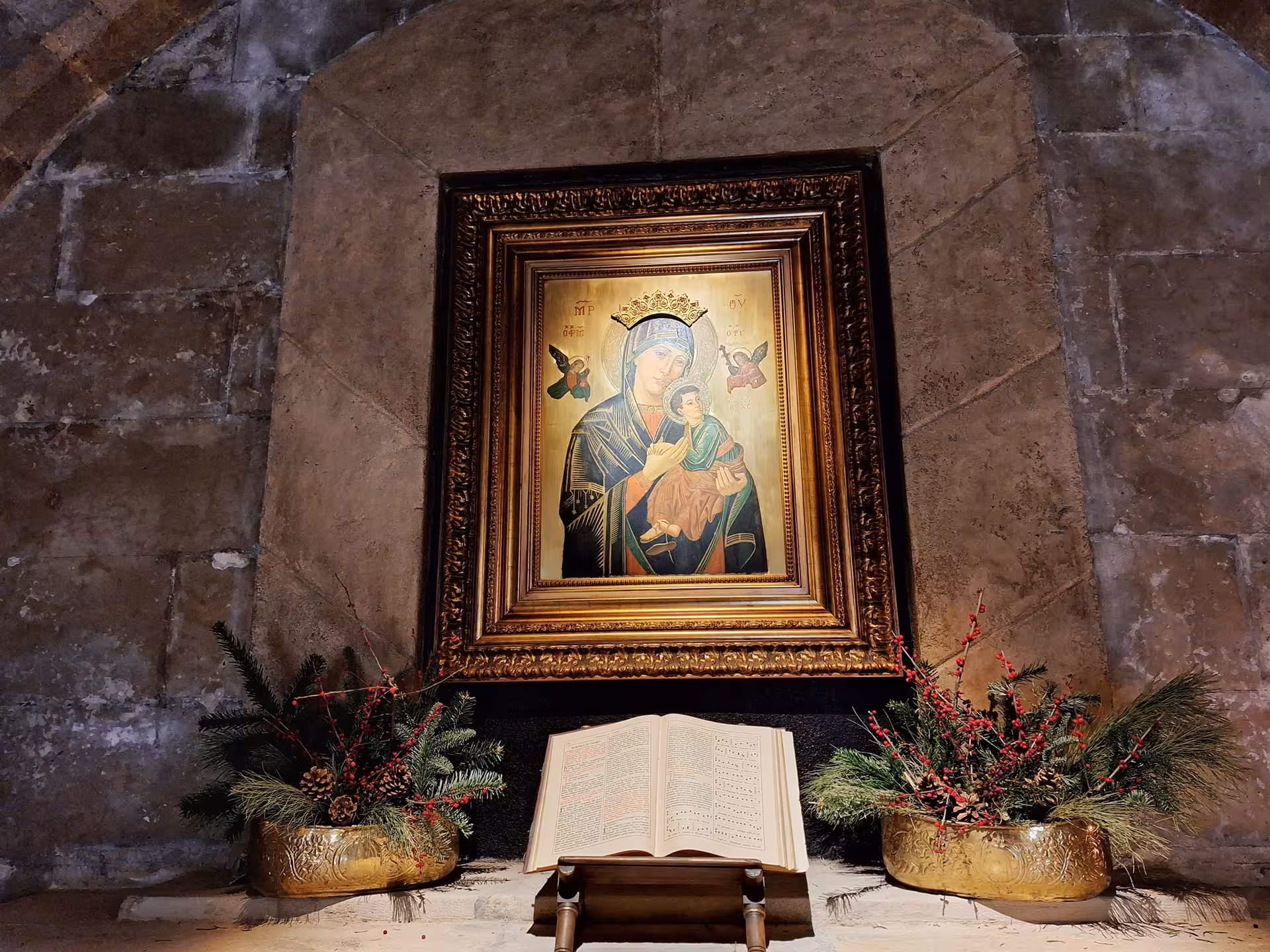 Ornate religious painting and open book in the Cathedral of Santander adorned with festive floral arrangements.