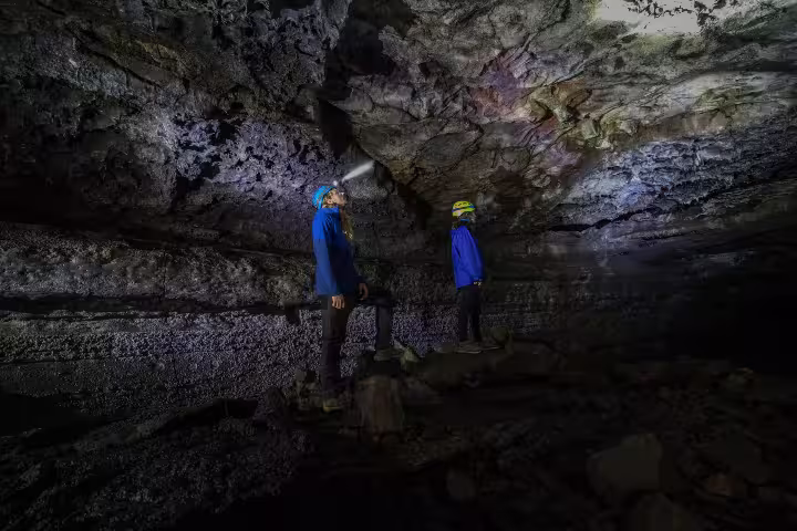 Explorers with helmets and headlamps stand inside Leidarendi Lava Tunnel, showcasing Iceland's stunning volcanic formations.