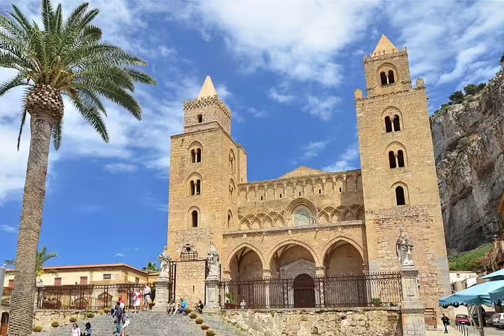 Tourists climbing steps to Cefalù Cathedral, a Norman-Arab church with twin towers and palm tree backdrop on Sicily excursion