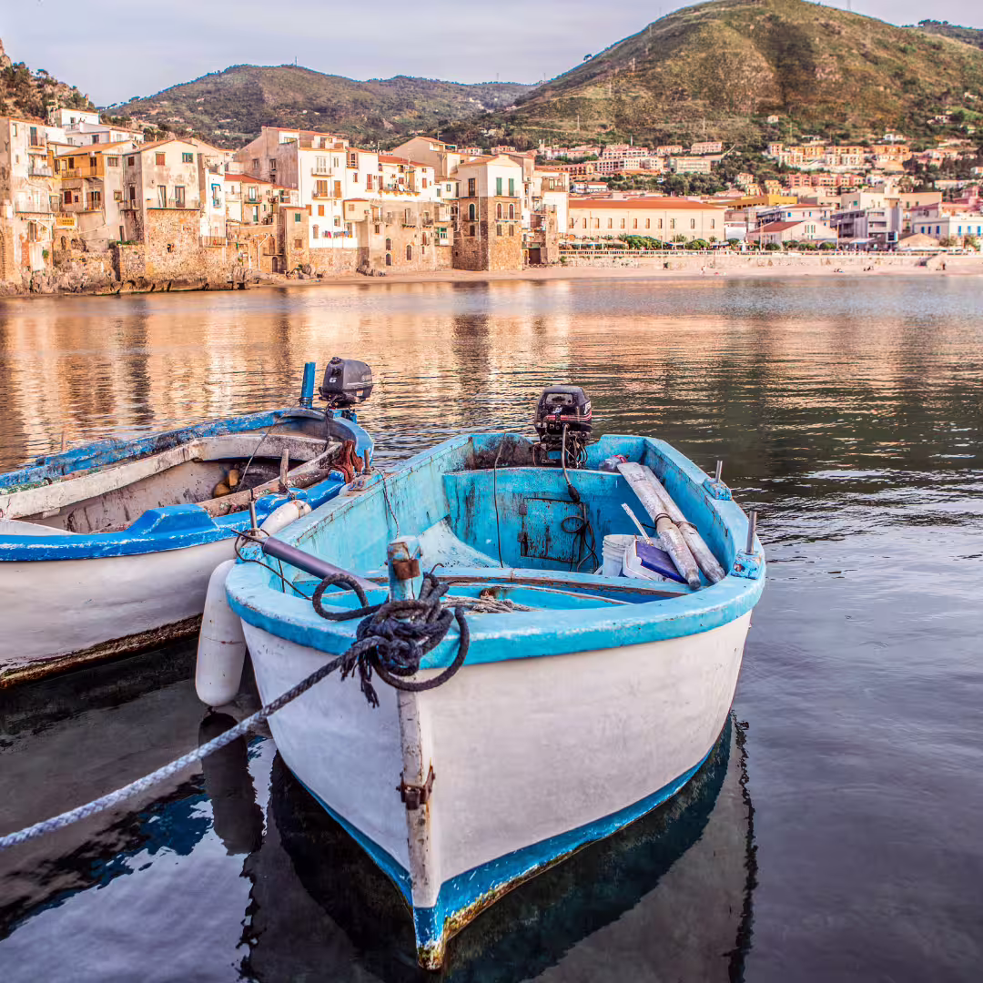 Traditional fishing boats in Cefalù harbor with medieval seafront houses and Madonie mountains on a Palermo day trip