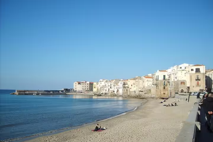 Sunny Cefalù beach with golden sand, calm Tyrrhenian Sea and historic seafront houses on a private day trip from Palermo