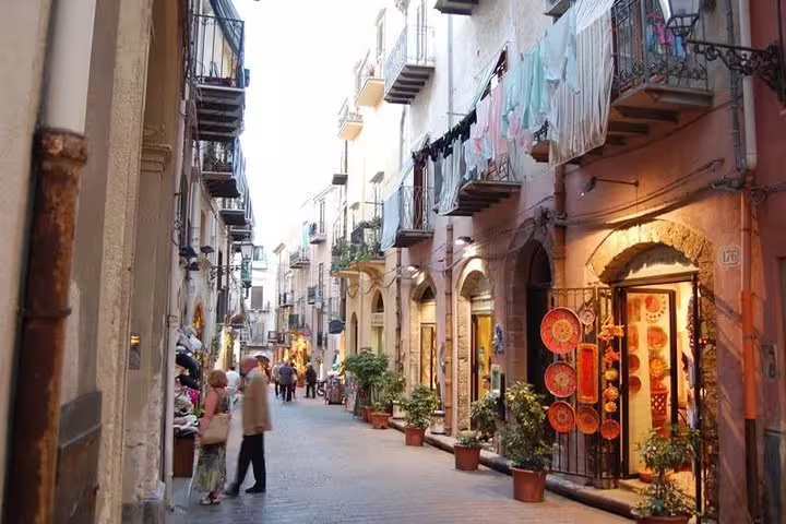 Charming narrow street in Cefalù with boutiques, balconies and locals on a private tour from Palermo