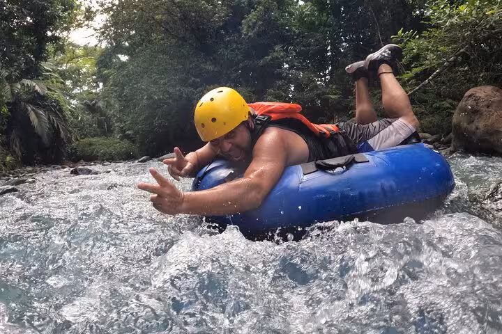 Adventurer enjoying thrilling tubing on the scenic Celeste River, surrounded by lush tropical rainforest.
