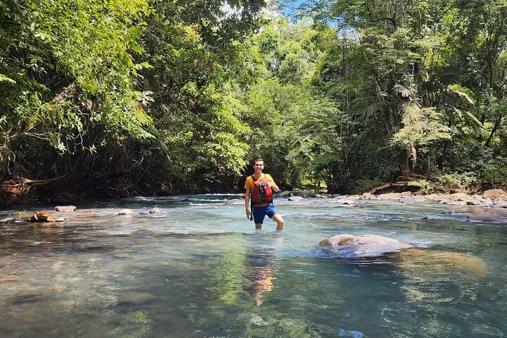 Traveler wading through the clear waters of the Celeste River amidst vibrant tropical greenery.
