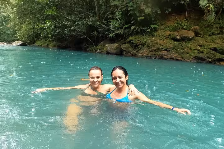 Two people enjoying a swim in the vibrant turquoise waters of the Celeste River surrounded by lush rainforest.