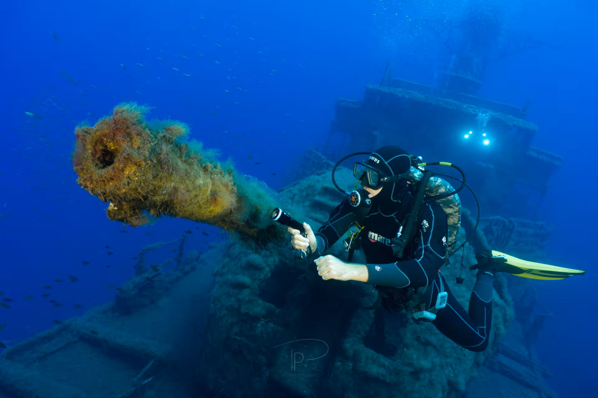 Diver exploring a shipwreck with a flashlight, highlighting underwater adventure for certified divers in clear blue waters.
