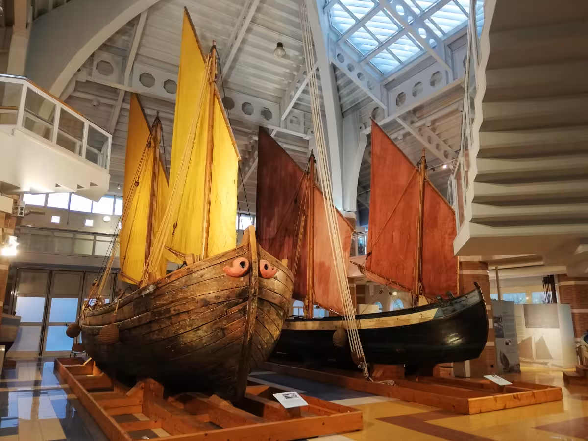 Historic wooden fishing boats on display at Cesenatico Maritime Museum indoor hall, colorful sails