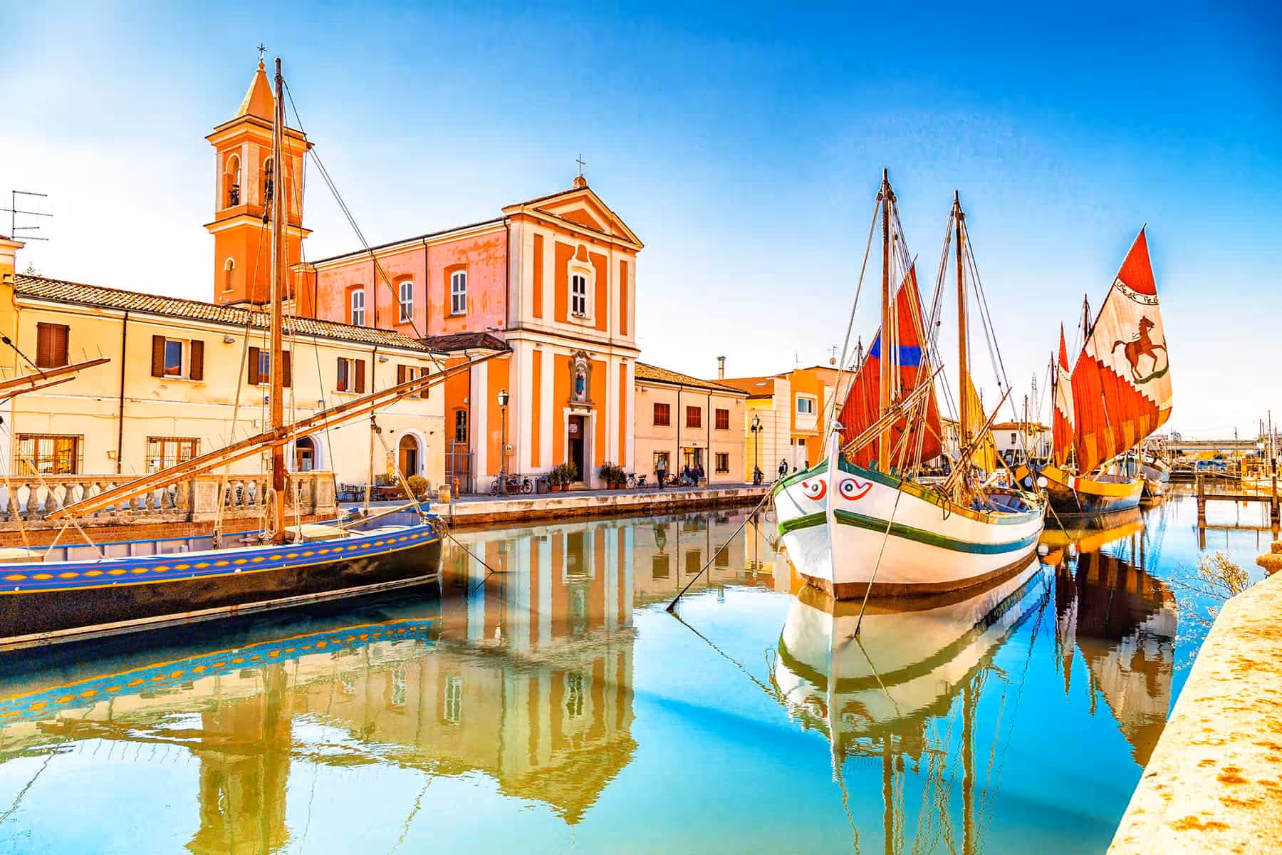 Traditional boats moored by Cesenatico canal and church, near Maritime Museum and Marino Moretti House visit