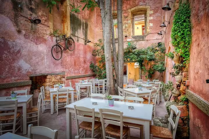 Charming outdoor café in Chania, Crete, with rustic pink walls and lush greenery, perfect for enjoying the West Crete private tour.