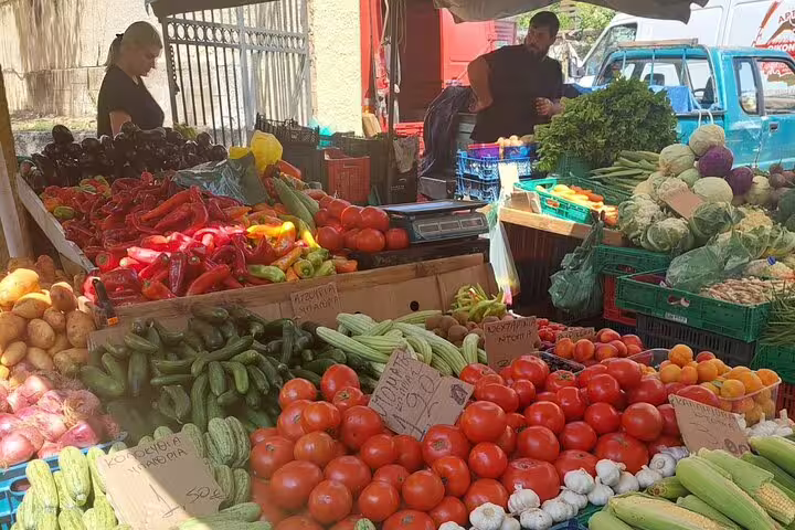 Colorful produce display at Chania's farmers market, featuring tomatoes, peppers, and zucchini under a sunny sky.