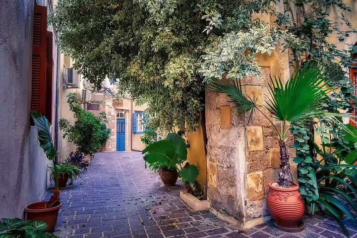 Charming narrow alley in Chania, Crete, adorned with lush greenery and vibrant potted plants, perfect for exploration.