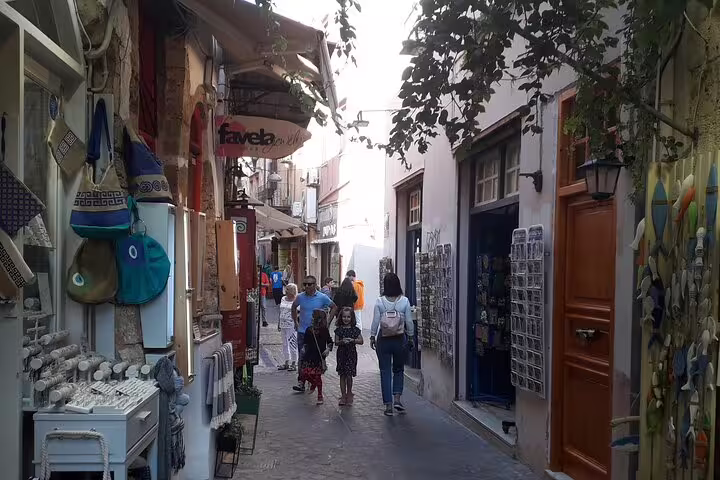 Tourists stroll through a charming narrow street in Chania, West Crete, lined with shops and vibrant local culture.