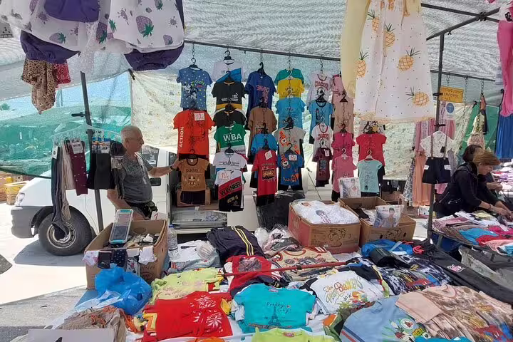 Colorful shirts and clothing on display at a bustling stall in Chania's Old Town market.