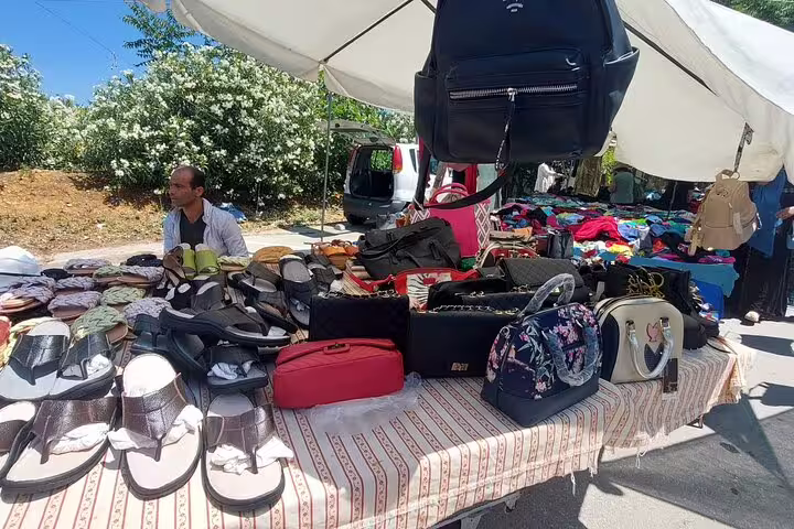 A variety of handbags and footwear displayed at Chania's lively Old Town market under a white canopy.