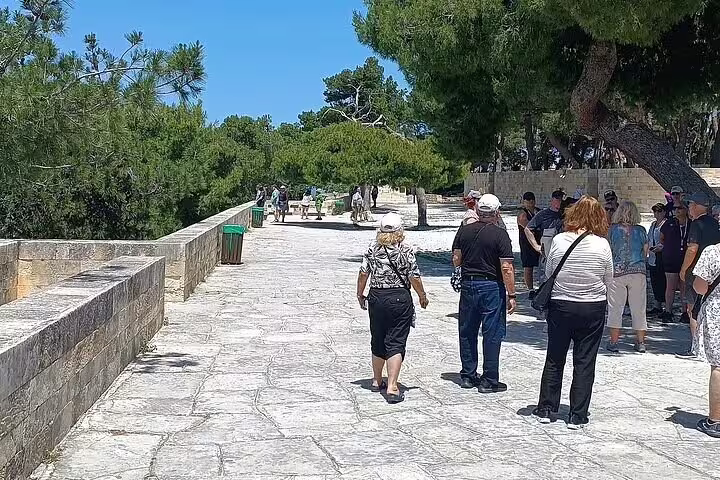 Tourists walk along the scenic path lined with lush trees in Chania's Old Town, enjoying the serene atmosphere.