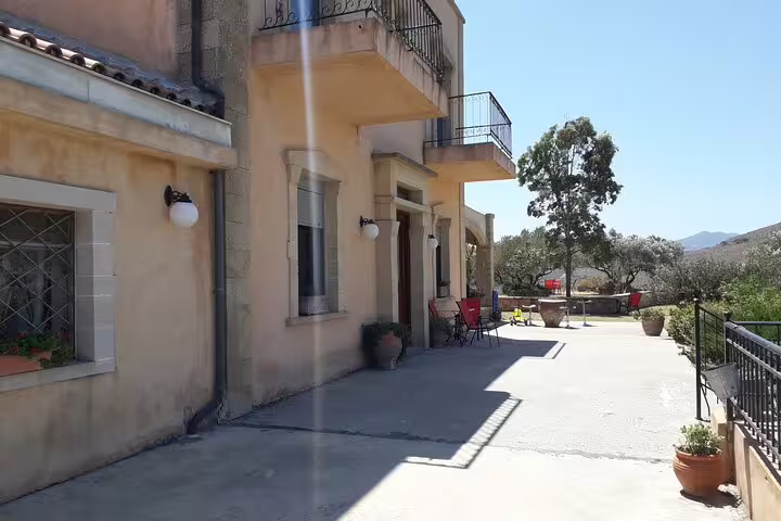 Sunny exterior view of Chania Old Town's traditional olive oil mill with inviting outdoor seating and olive trees.