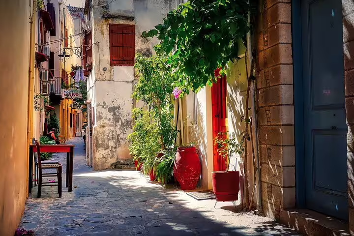 Idyllic sunlit alley in Chania with colorful doors, vibrant plants, and inviting local charm, ideal for a private tour.