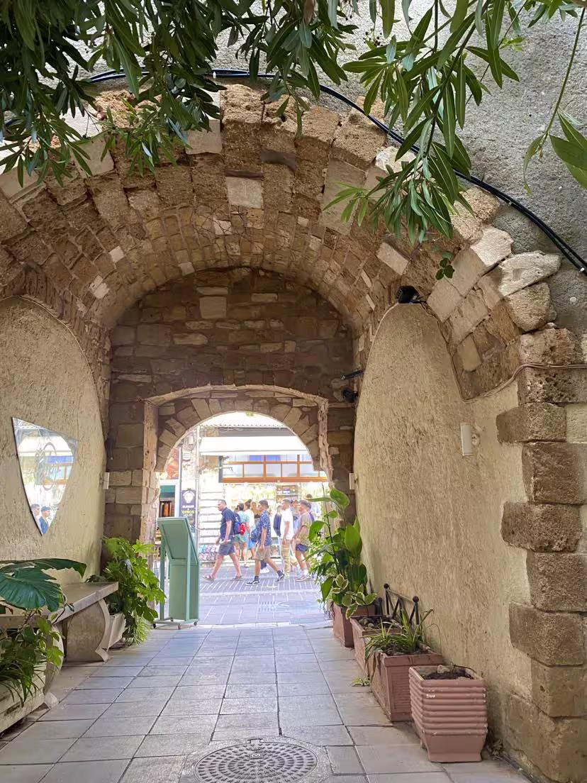 Charming stone archway in Chania with lush plants, leading to a vibrant street, perfect for semi-private tours.