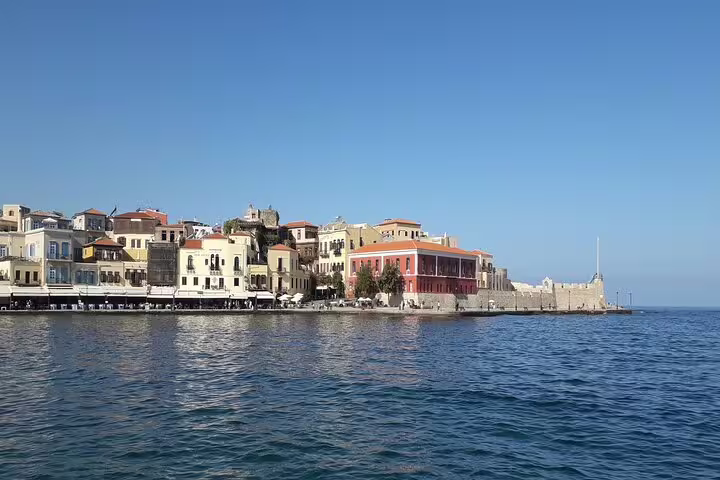 Scenic view of Chania's Old Venetian Harbor in Crete with colorful waterfront buildings under a clear blue sky.