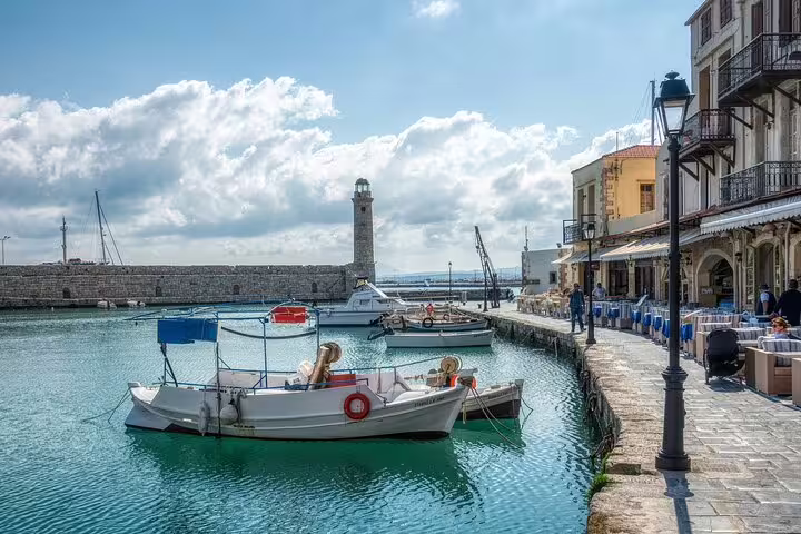Scenic view of Chania's Venetian harbor with boats, lighthouse, and waterfront cafes, ideal for West Crete private tours.