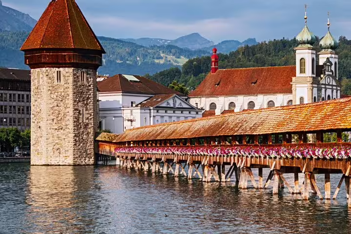 Iconic Chapel Bridge in Lucerne adorned with flowers, with the backdrop of historic buildings and Mount Pilatus.