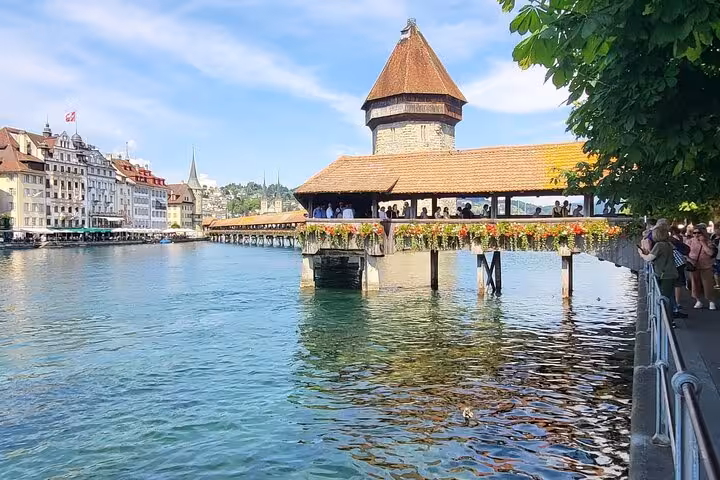 Chapel Bridge in Luzern adorned with flowers, reflecting on the Reuss River under a clear blue sky.