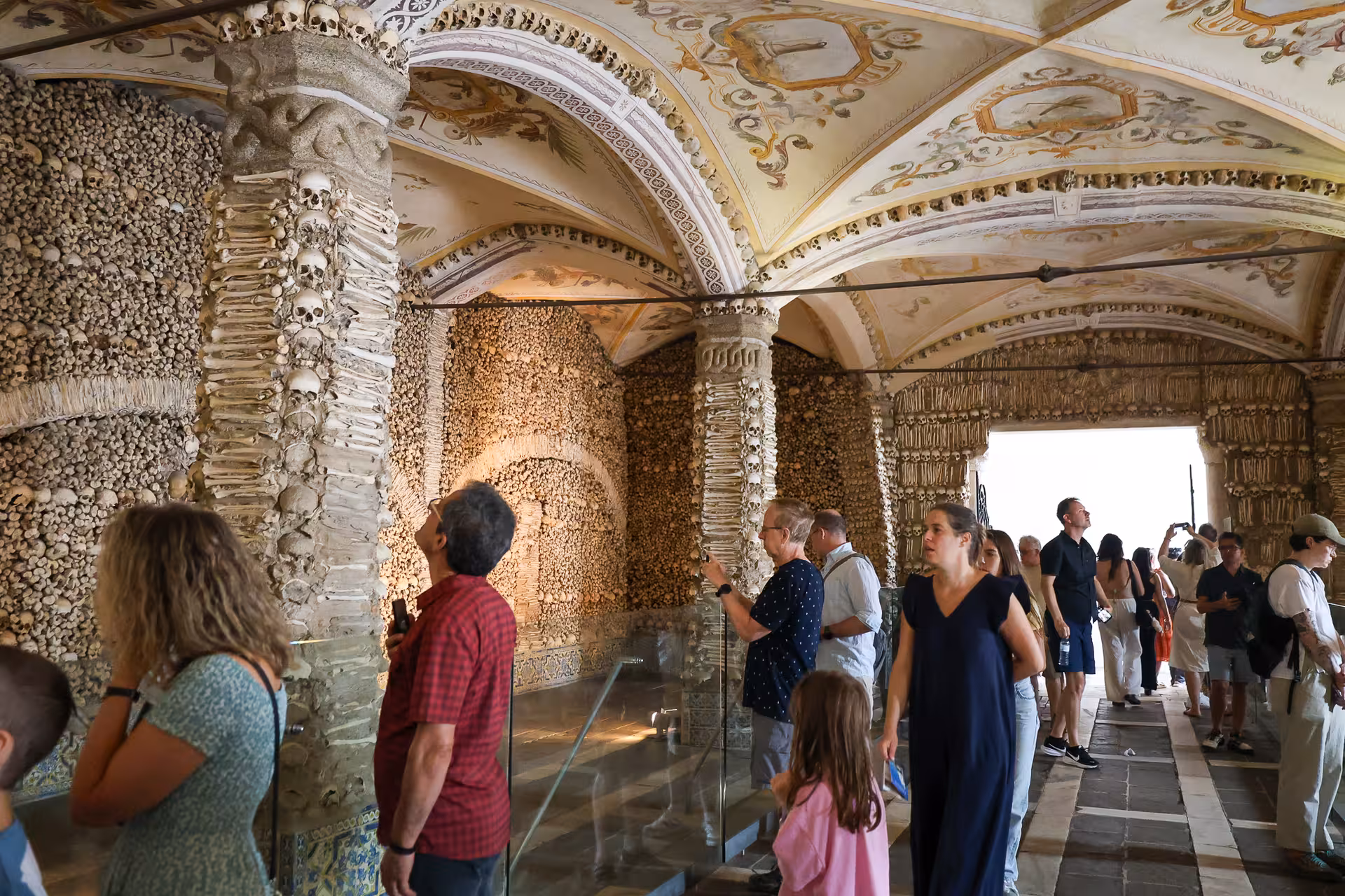 Visitors exploring the historic Chapel of Bones in Évora, adorned with human skulls and bones.