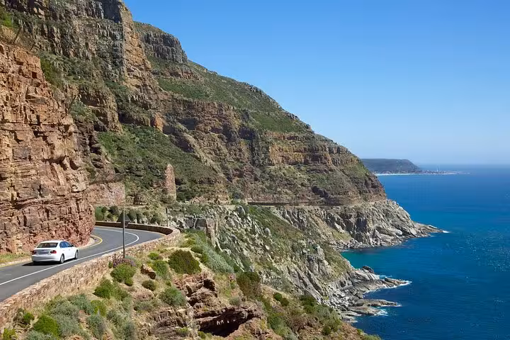 Car driving along picturesque Chapman's Peak Drive with ocean and cliff views, Cape of Good Hope adventure.