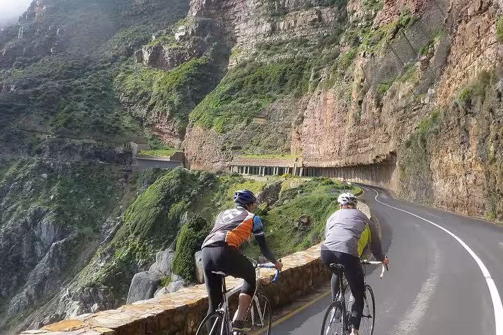 Cyclists enjoying a breathtaking ride along Chapman's Peak Drive, surrounded by lush cliffs on the Cape of Good Hope tour.