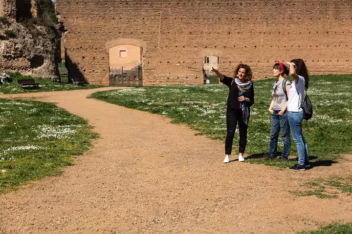 Tour guide explaining ancient ruins to travelers on a sunny day along the historic Appian Way in Rome.