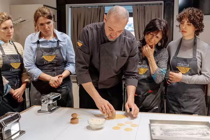 Chef demonstrates corzetti pasta stamping technique to engaged participants at MaMa Florence class.