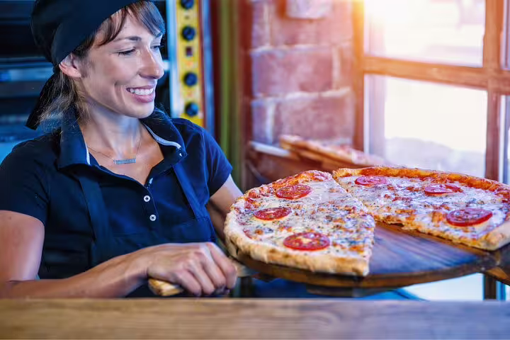 Smiling chef presenting freshly baked Italian pizza on a wooden paddle, highlighting the Italian Aperitivo Foodie Tour experience.