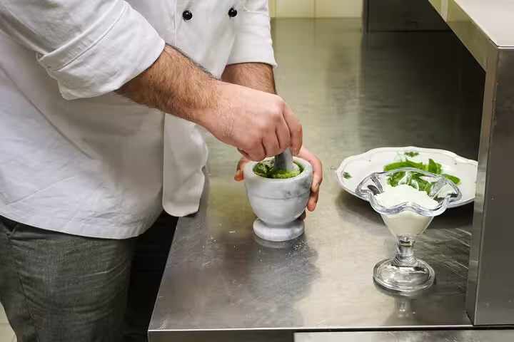 Chef prepares fresh pesto sauce with mortar and pestle in a Rome cooking class featuring authentic Italian ingredients.