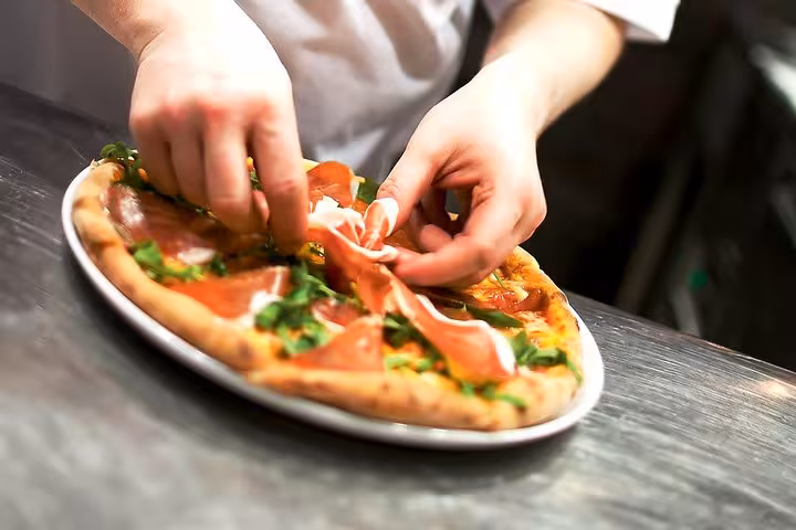 Chef expertly preparing a gourmet pizza with fresh toppings in a Florence cooking class experience.