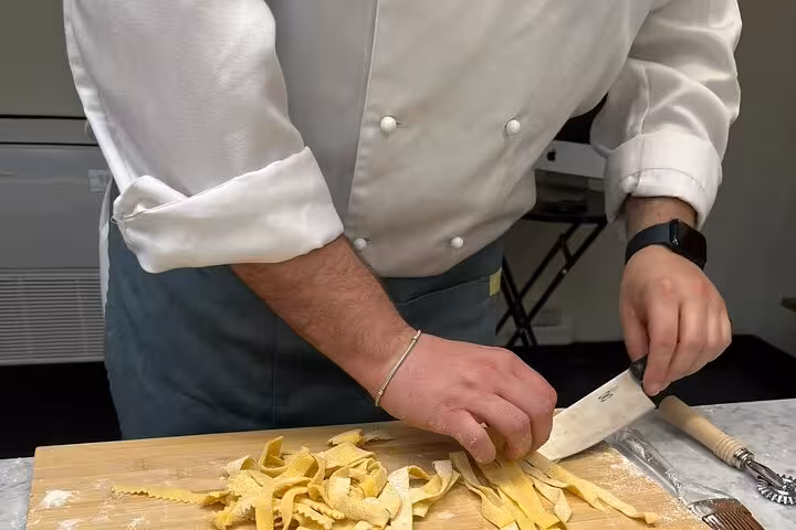 Chef skillfully slicing homemade fettuccine pasta on a wooden board, showcasing traditional Italian cooking techniques.