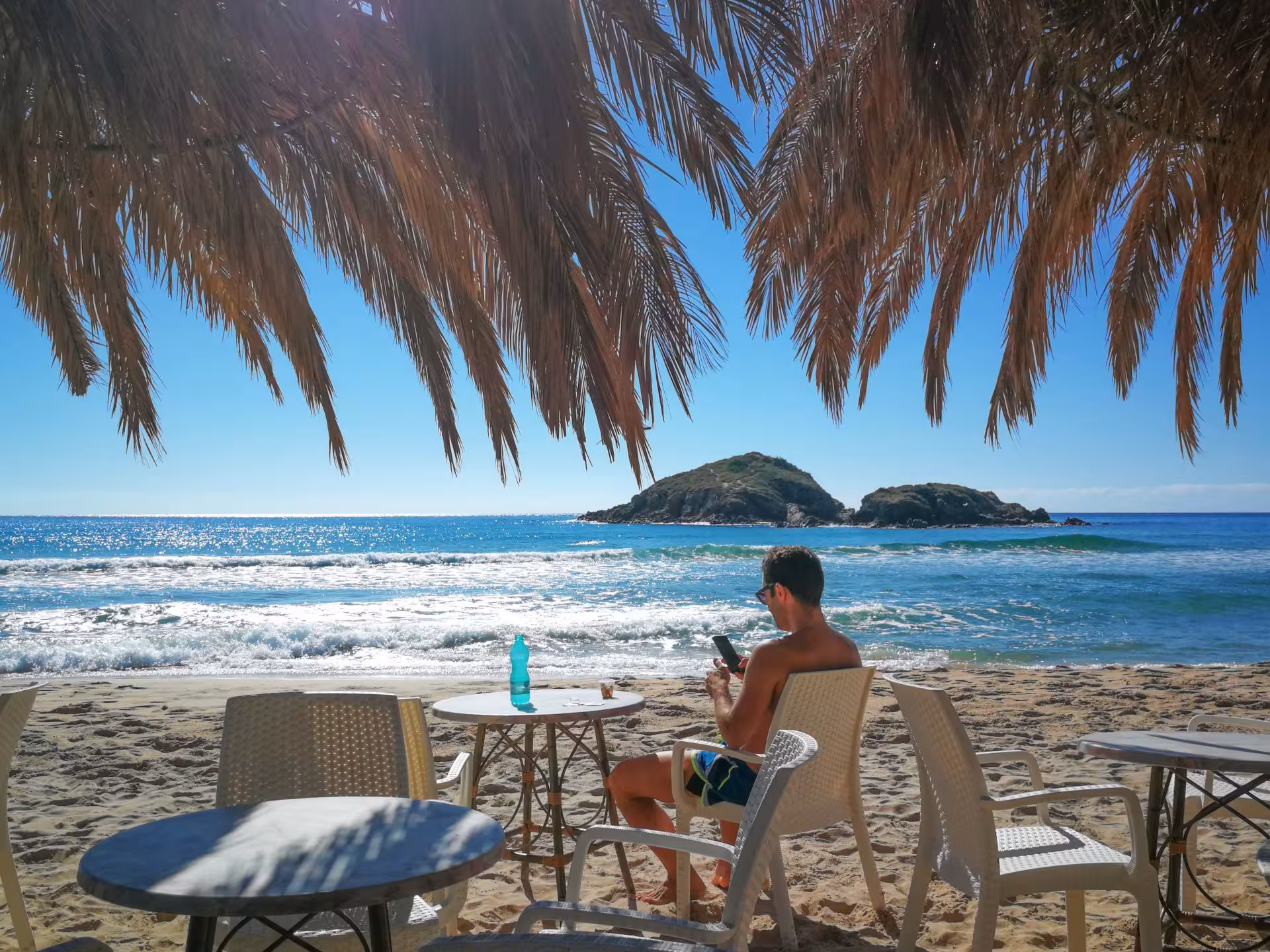 Relaxed tourist enjoying a sunny day under palm shade at Chia Beach, with clear blue sea and distant islands.