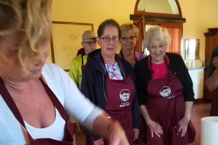 Travelers in aprons watch a local chef during a hands-on Tuscan cooking class on a Chianti countryside walking tour