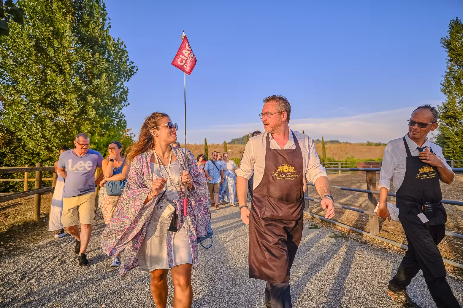 Tourists walking with guide in Chianti vineyard, holding a flag, on Siena wine tour.