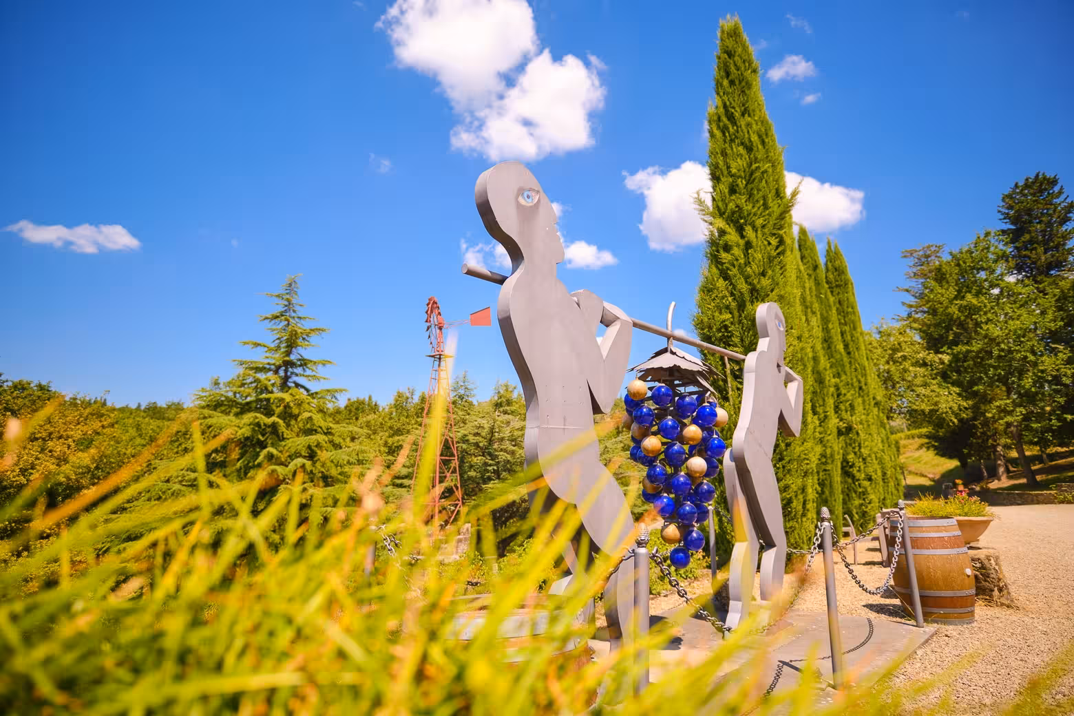 Artistic sculpture of figures carrying grapes under a clear blue sky in the scenic Chianti wine region.