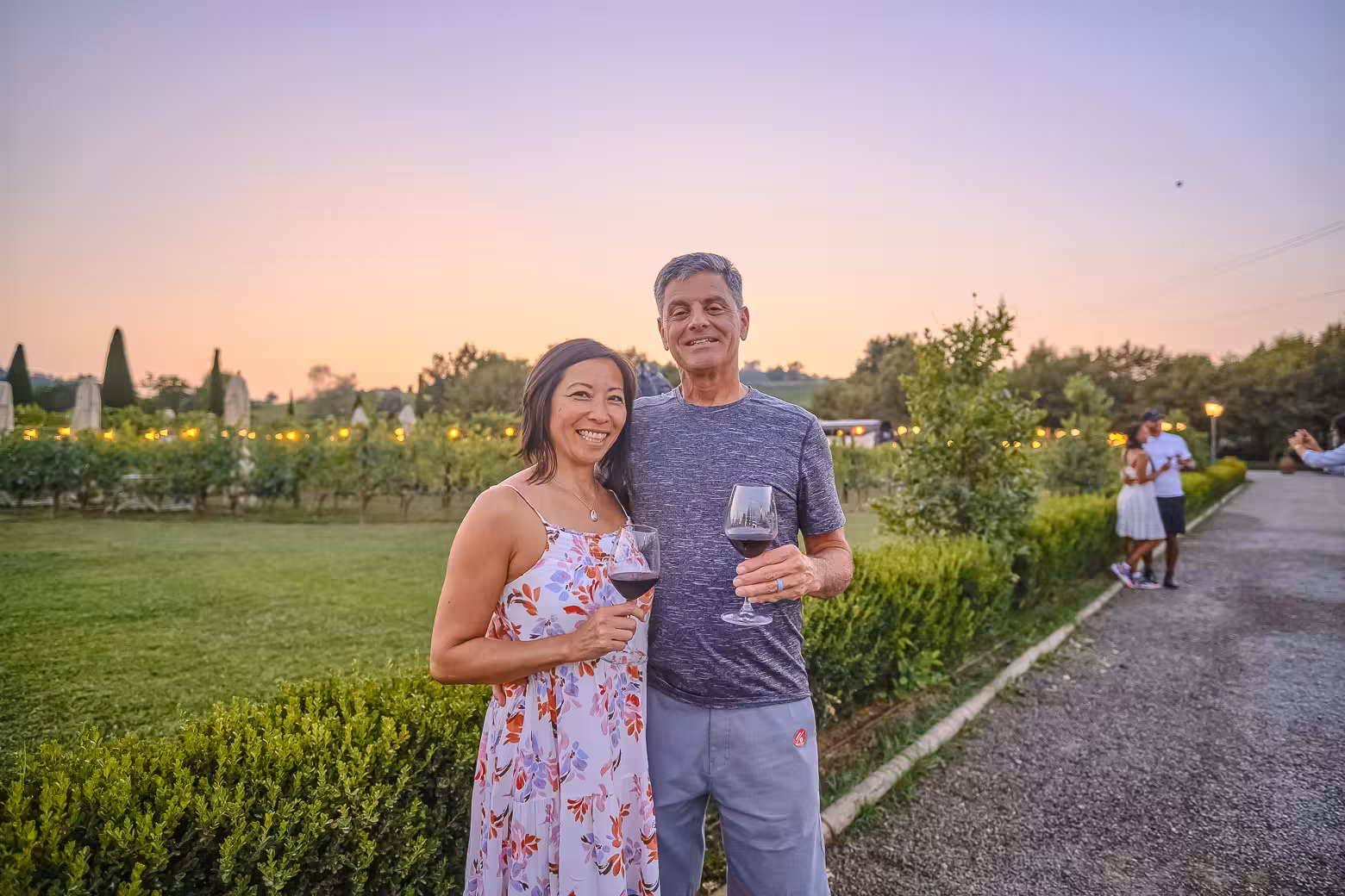 Couple enjoying Chianti winery tour with wine glasses at sunset, experiencing Tuscany's vineyard charm.