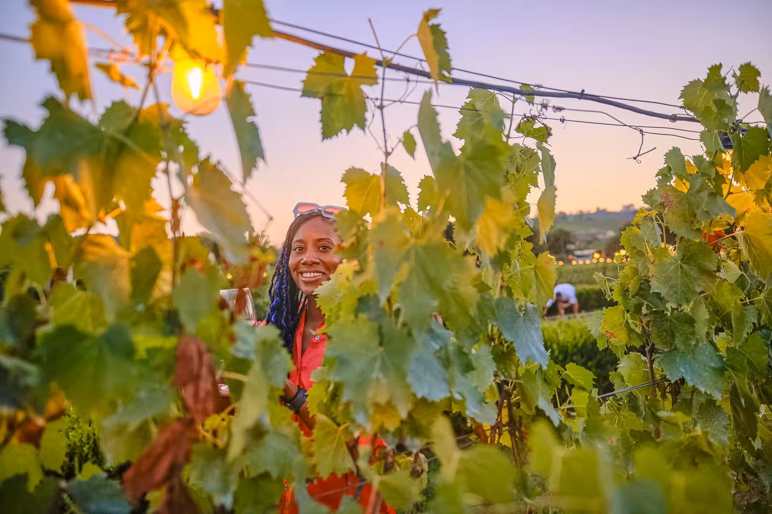 Smiling visitor enjoys a sunset wine tasting amidst lush Chianti vineyard vines on a small-group tour.