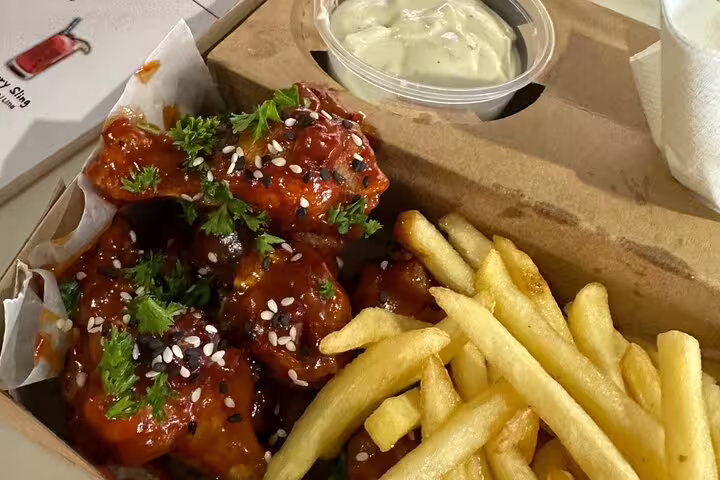 Delicious chicken wings with sesame seeds and parsley, served with crispy fries and creamy dip on a food tour.