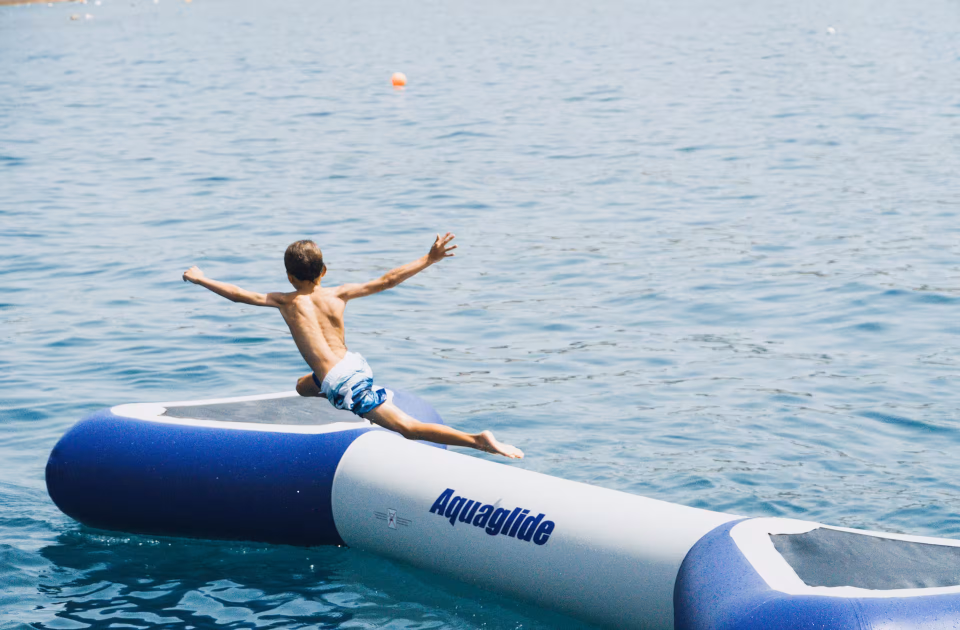 Excited child sliding off an Aquaglide inflatable into clear blue sea on a fun catamaran tour in Lagos.