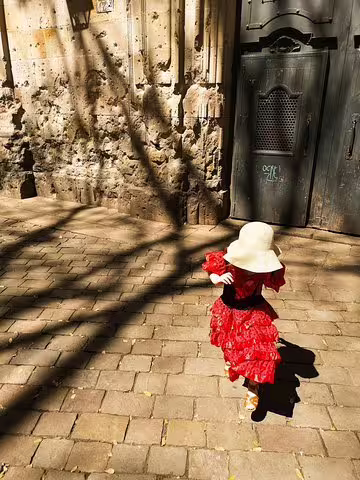 Child in red dress and sunhat explores a historic Barcelona street, highlighting family-friendly tours with churros and games.