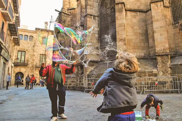 A child joyfully plays with giant bubbles in a historic Barcelona square, perfect for a family tour with churros and hot chocolate.