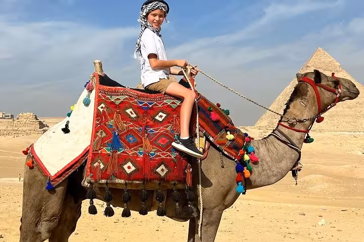 Child on a decorated camel near the Pyramids of Giza, ideal for full-day tour with hotel pickup from Cairo